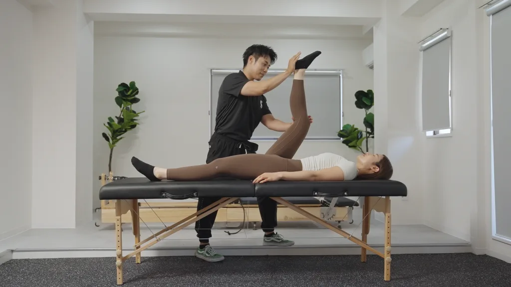 施術ベッドの上で、トレーナーがお客様の脚をストレッチしてほぐしている様子