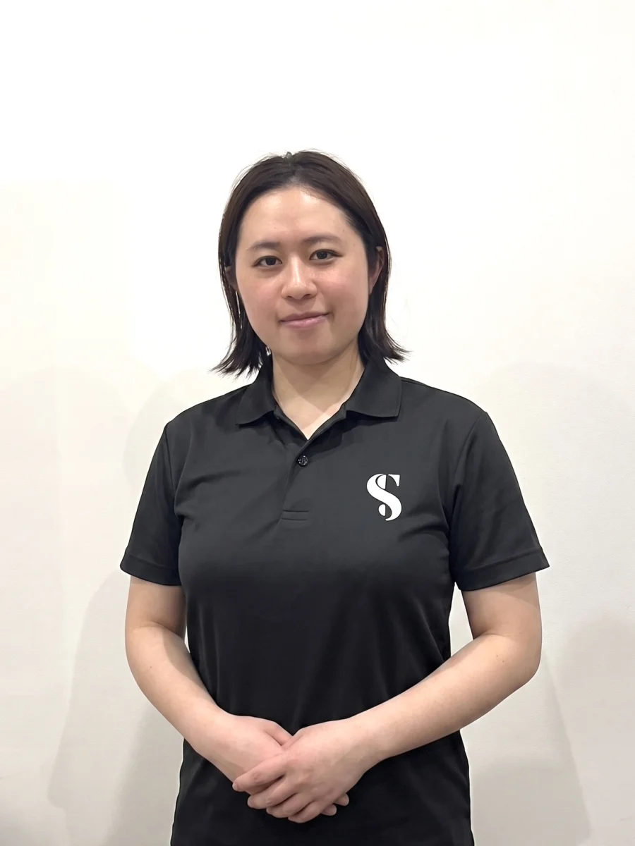 黒いSTLINEポロシャツを着て正面に立つ女性トレーナー